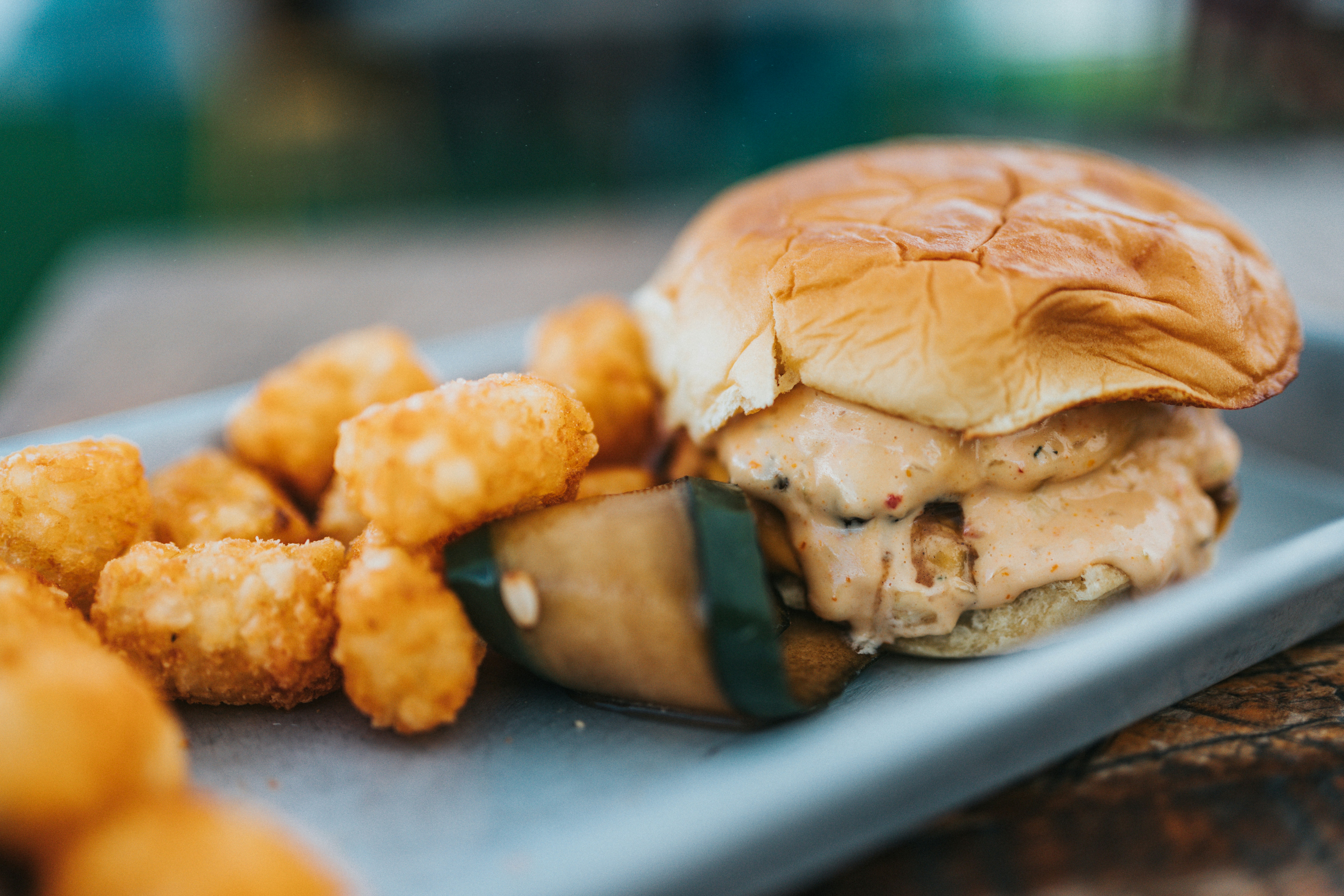 A burger and crispy tater tots being served on a metal tray.