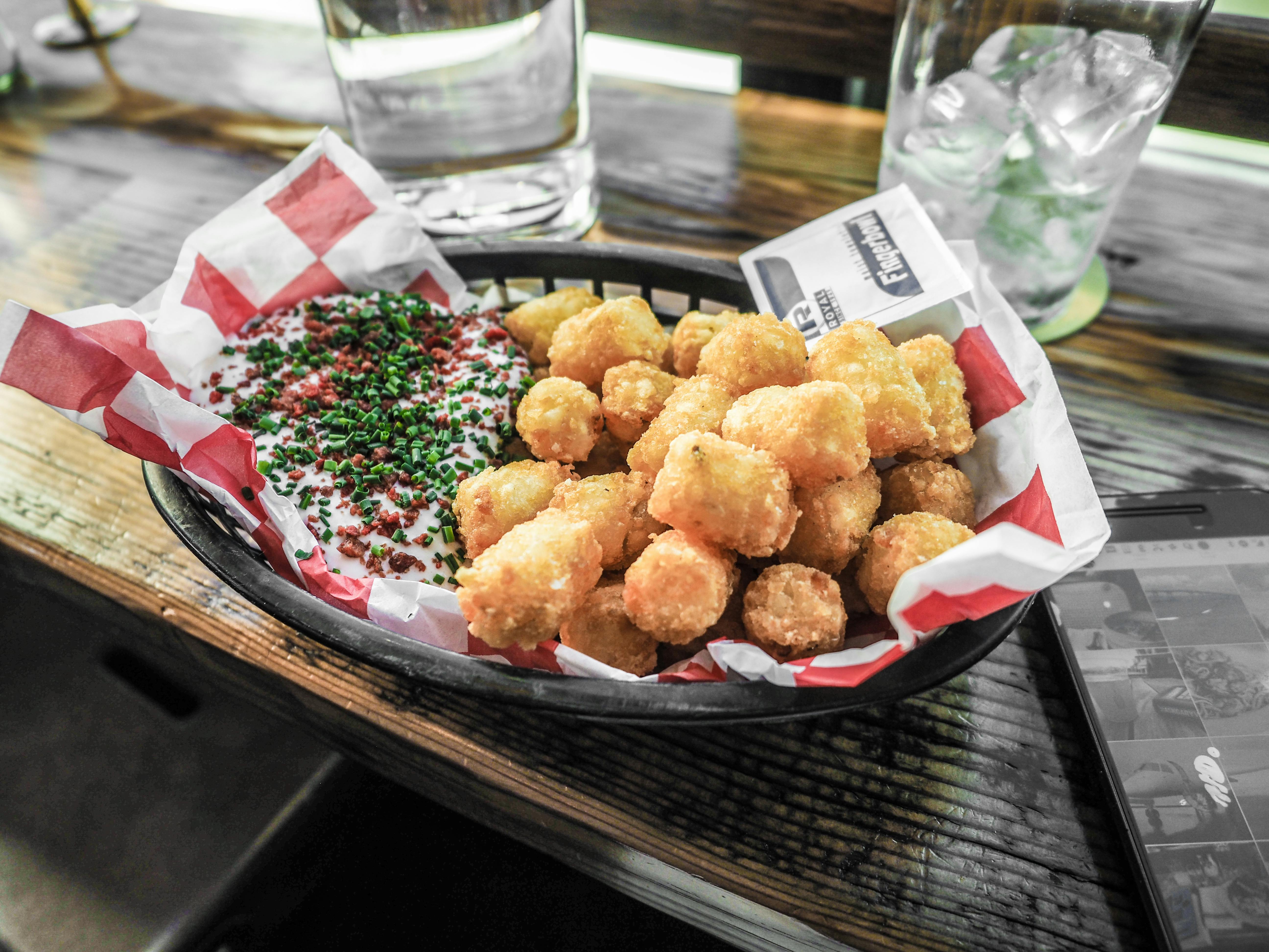 A basket of crunchy tater tots served with a sour cream dip.