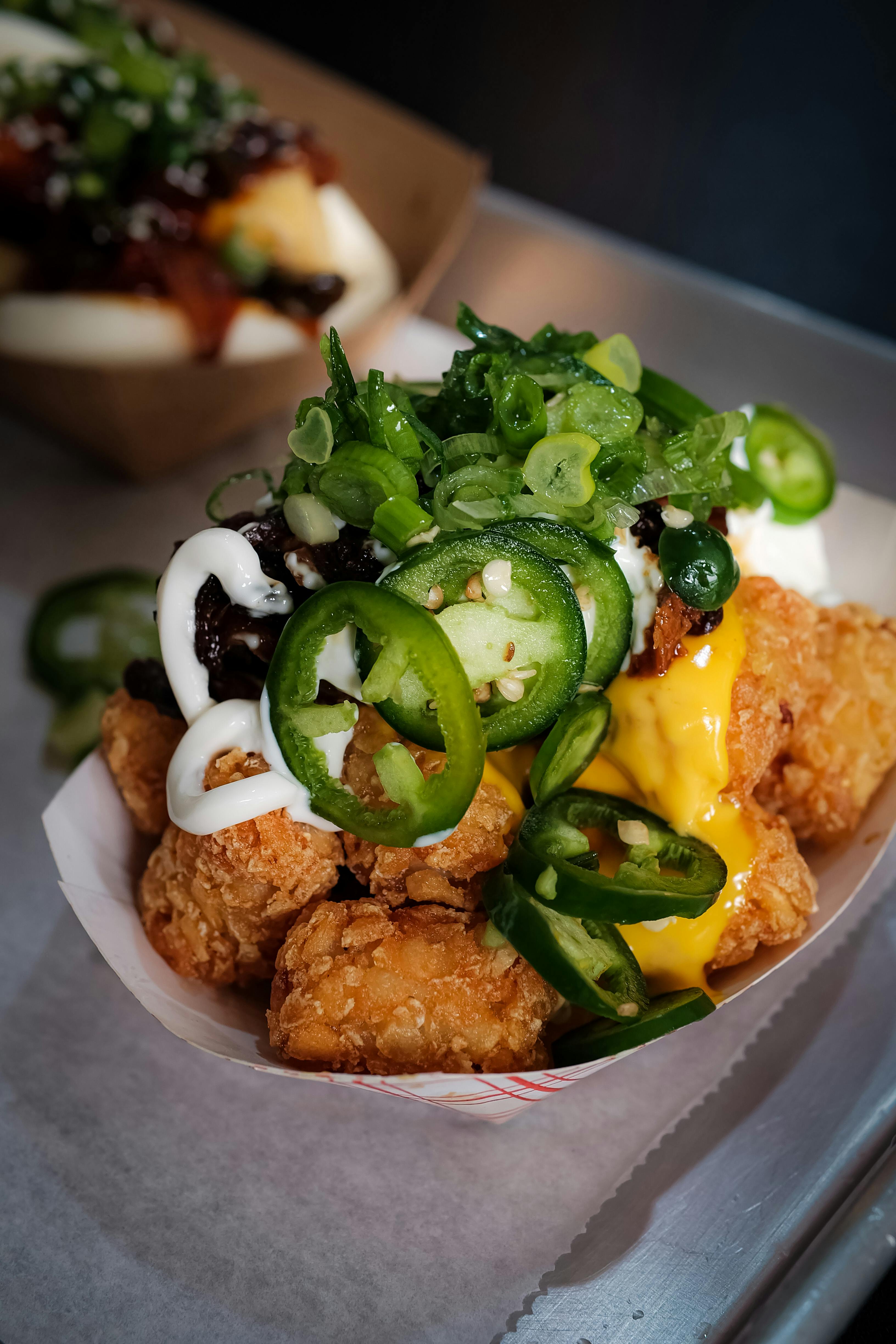 A bowl of tater tots topped with jalapenos and other mouth watering toppings.